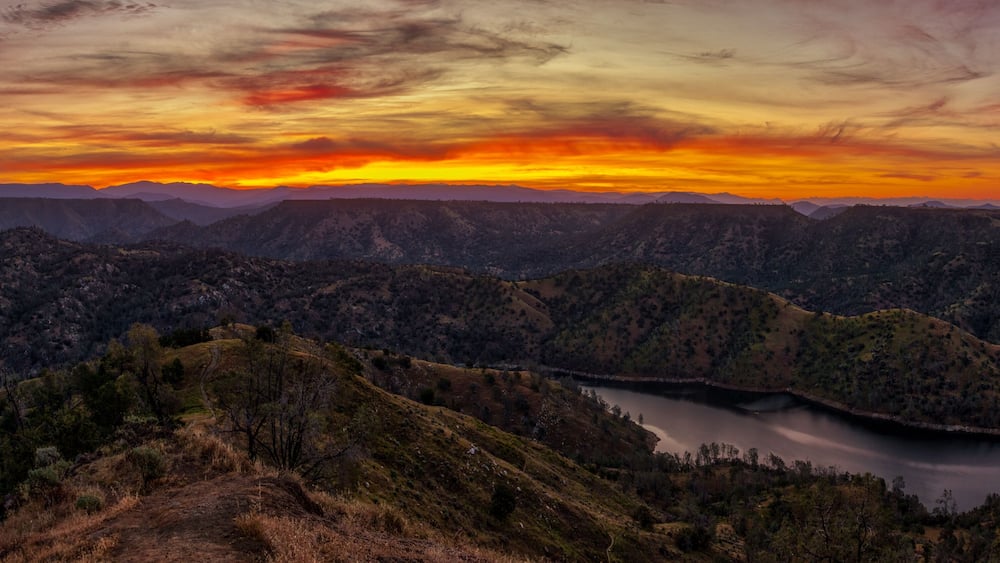 Paisagem montanhosa com um lago e um pôr do sol.