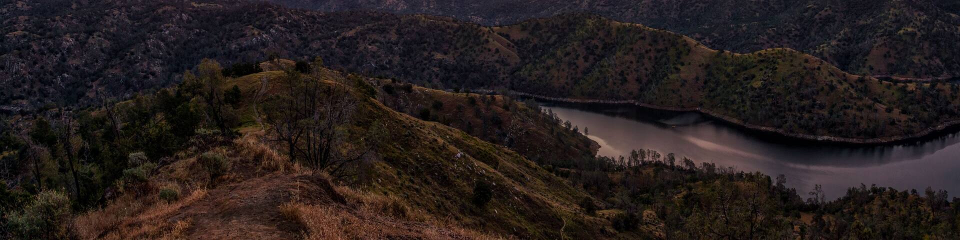 A mountainous landscape with a lake and a sunset.