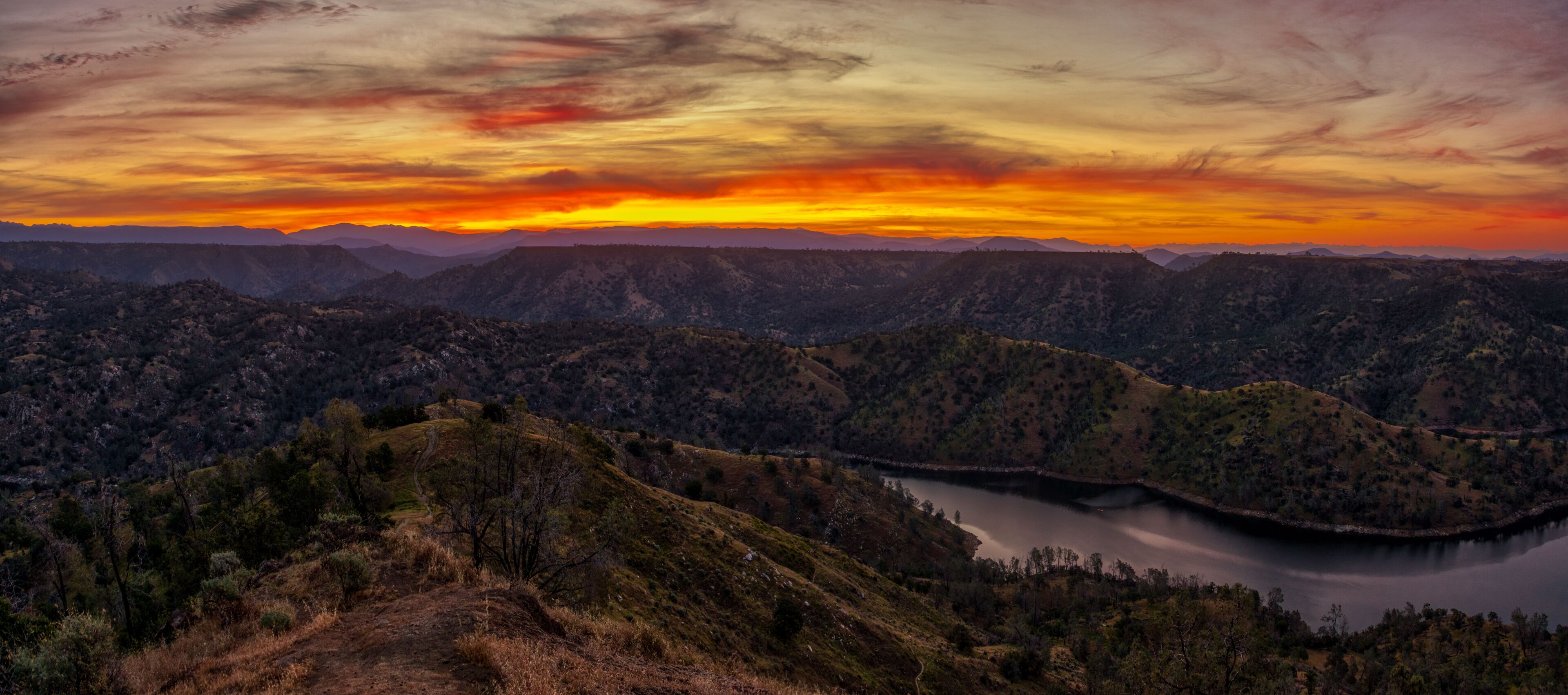 A mountainous landscape with a lake and a sunset.