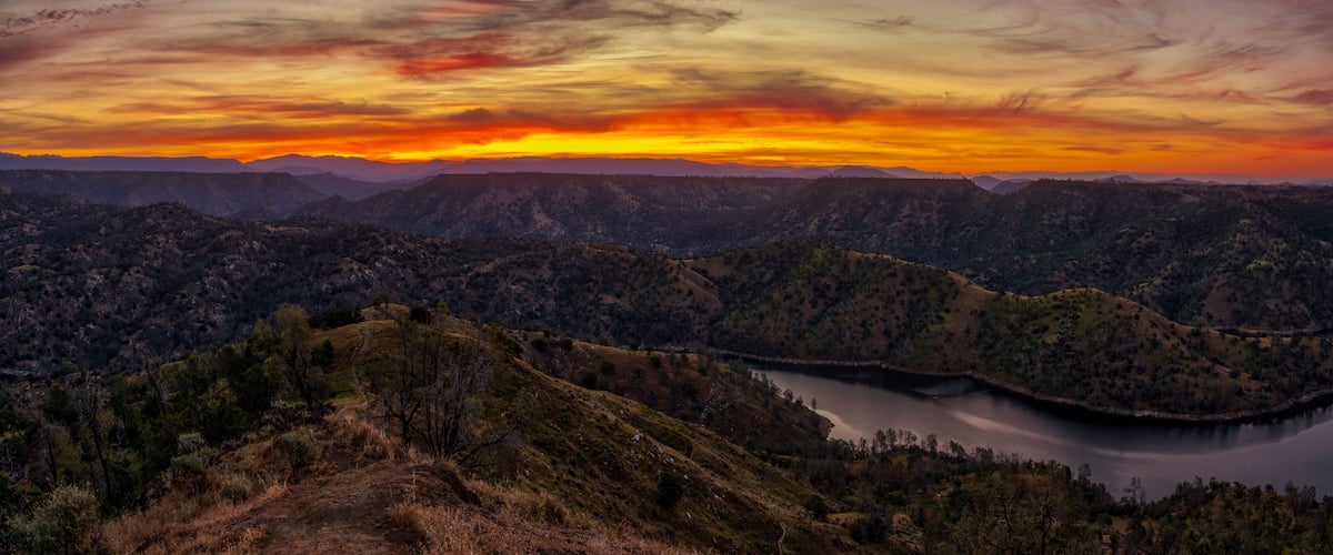 A mountainous landscape with a lake and a sunset.