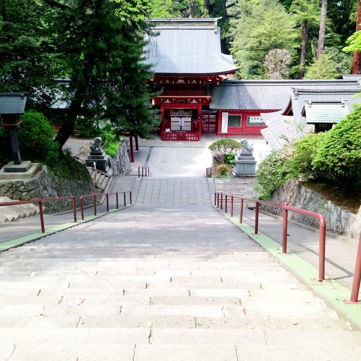 A traditional Japanese temple with a red gate, stone steps, and surrounding greenery.
