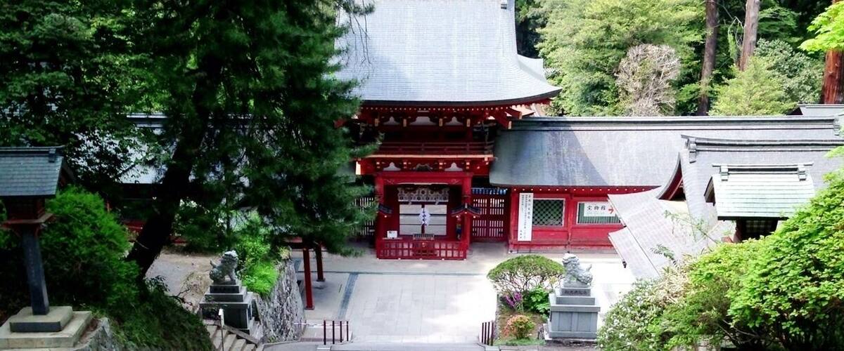 A traditional Japanese temple with a red gate, stone steps, and surrounding greenery.