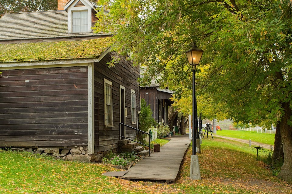 A wooden cabin with a moss-covered roof, a wooden porch, and a street lamp.