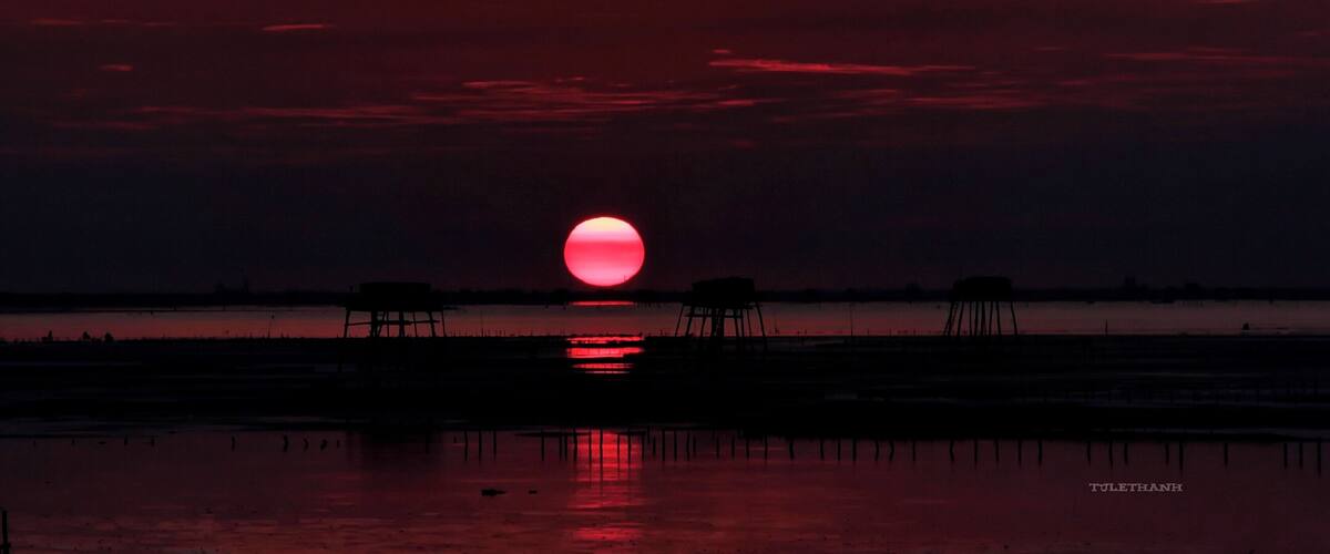 A sunset over a calm water body with a red sky.