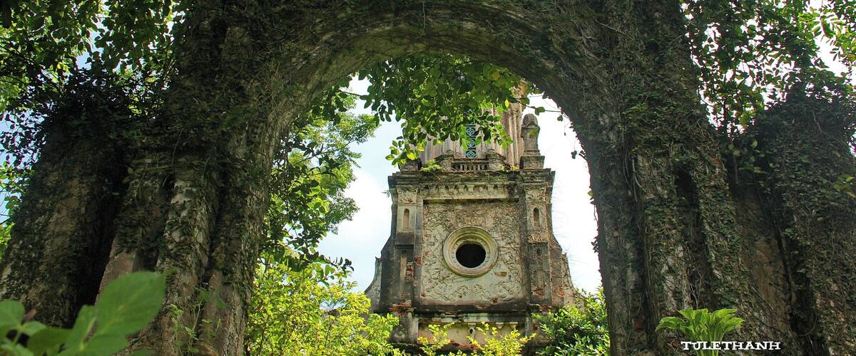 An ancient stone structure with a circular window, surrounded by dense foliage and an archway.