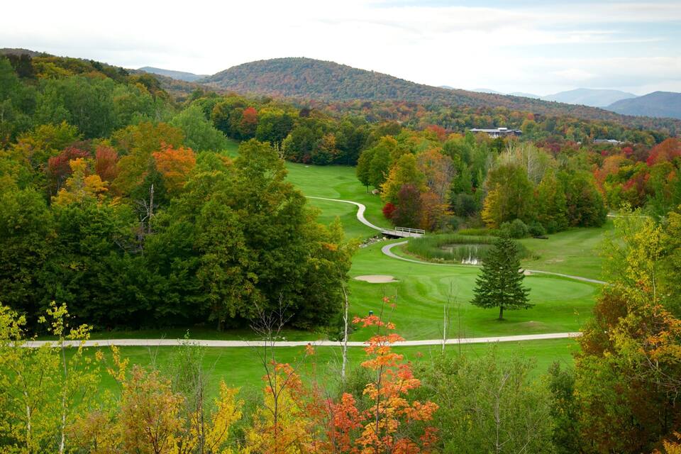 A golf course surrounded by autumn-colored trees and hills.