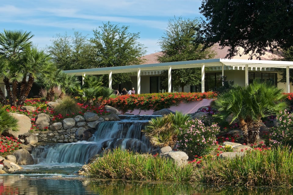 A waterfall, rocks, and a covered walkway in a garden.