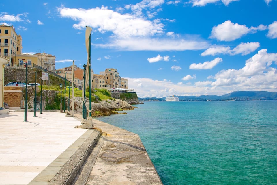 Um calçadão à beira-mar com edifícios, um cais e um cruzeiro ao longe.