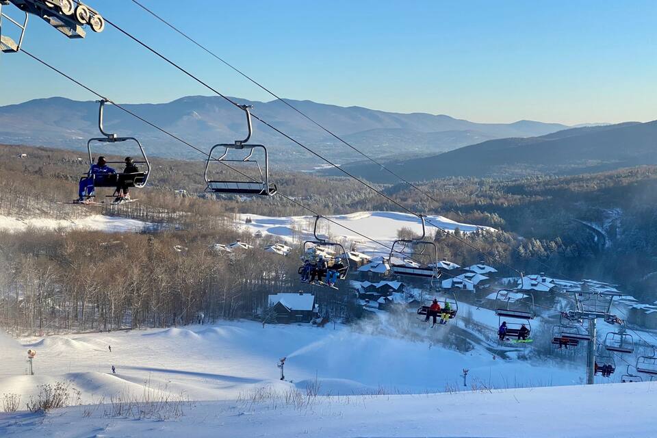 A ski lift with skiers, a snowy landscape, and distant mountains.