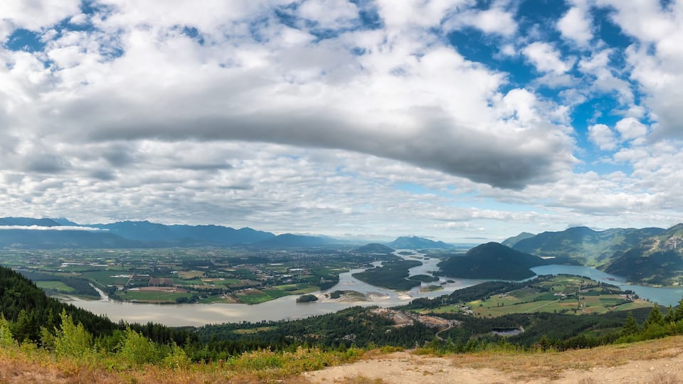 A panoramic view of a valley with a river, mountains, and a forested area.