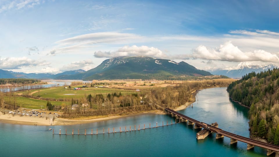 A river with a bridge, surrounded by mountains and forest.