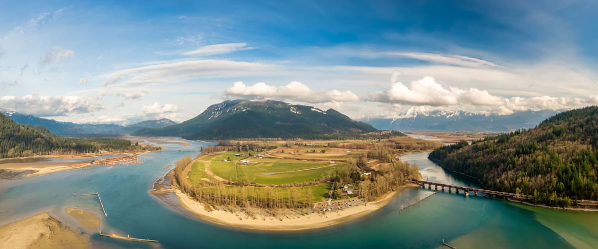 Aerial Panoramic View of a River in the valley surrounded by Canadian Mountain Landscape. Green Farms. Taken in Harrison Mills, Fraser Valley, East of Vancouver, BC, Canada.
