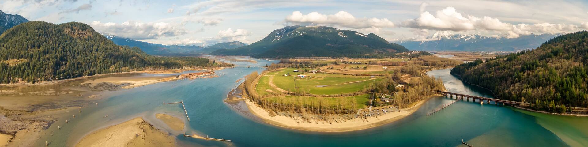 Aerial Panoramic View of a River in the valley surrounded by Canadian Mountain Landscape. Green Farms. Taken in Harrison Mills, Fraser Valley, East of Vancouver, BC, Canada.