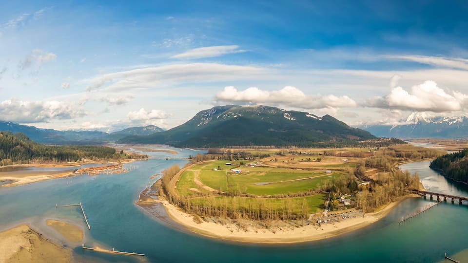 A river winding through a valley with mountains in the background and a bridge crossing the river.