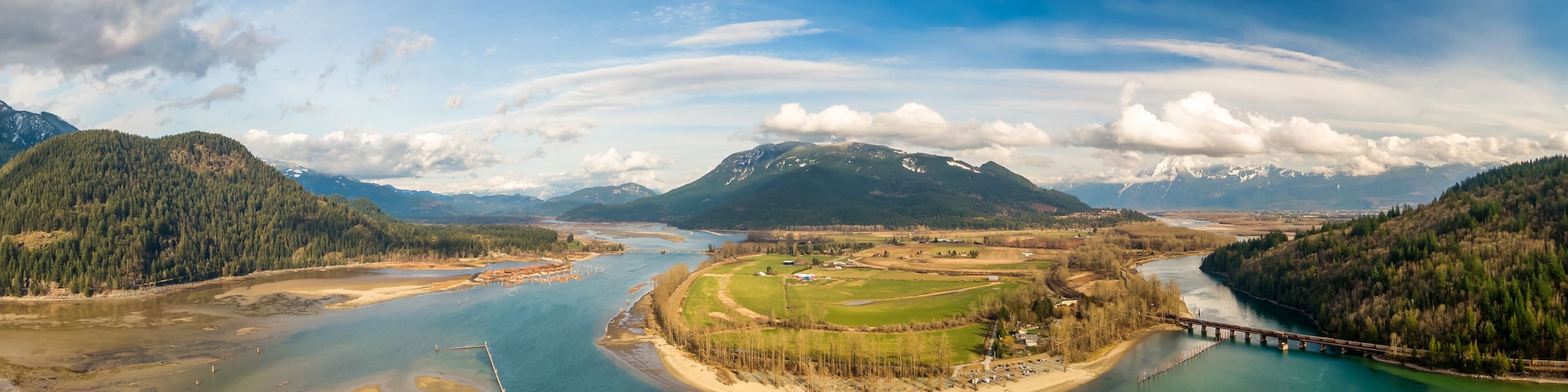 Aerial Panoramic View of a River in the valley surrounded by Canadian Mountain Landscape. Green Farms. Taken in Harrison Mills, Fraser Valley, East of Vancouver, BC, Canada.
