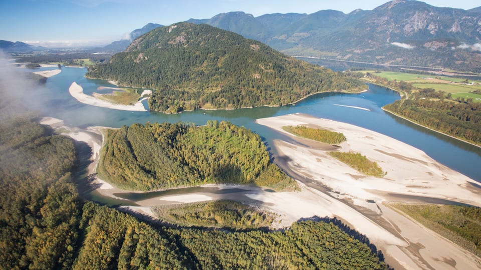 A river winding through a forested valley with mountains in the background.