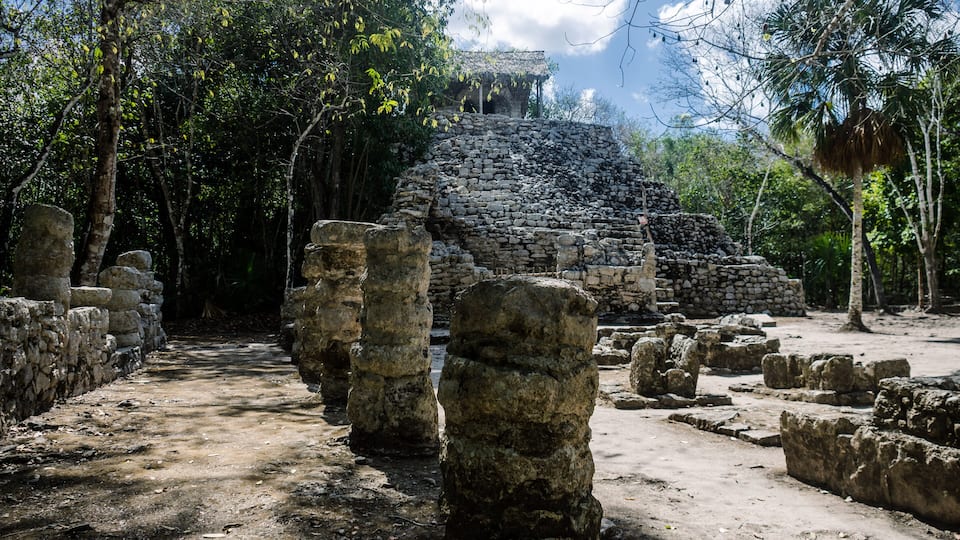 Ancient stone ruins with a staircase leading to a temple, surrounded by dense tropical foliage.