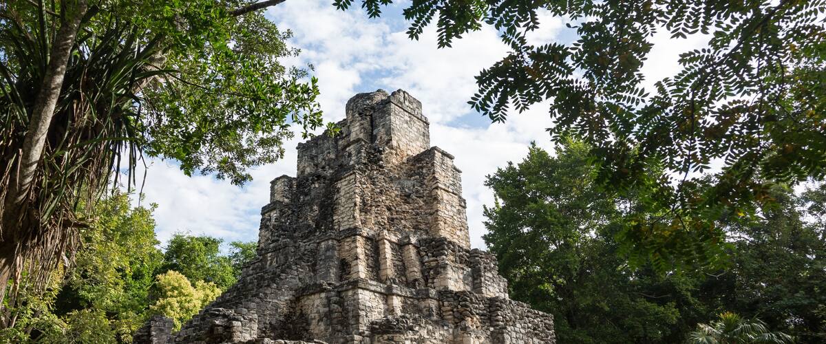 An ancient stone pyramid surrounded by lush greenery.