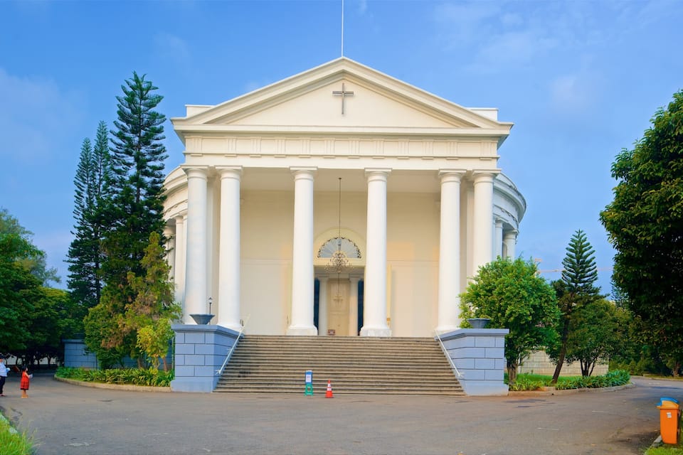 Um edifício neoclássico com uma cúpula central e colunas, rodeado por árvores e um céu claro.