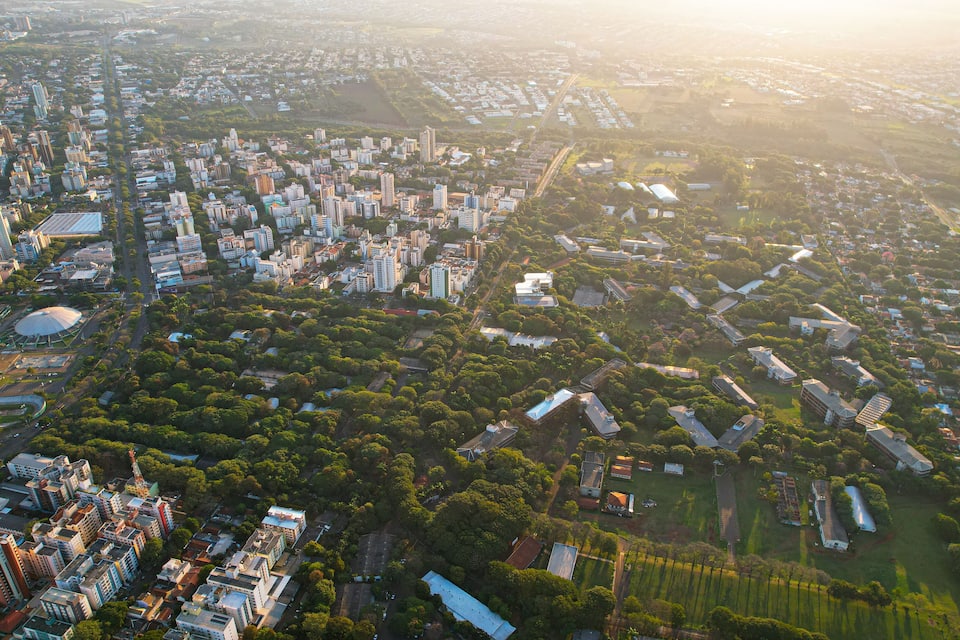 Vista aérea de uma cidade com áreas urbanas densas, áreas verdes e uma mistura de edifícios residenciais e comerciais.
