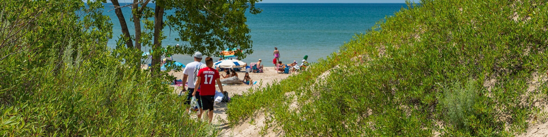 Una playa con gente tomando el sol y caminando por la orilla.
