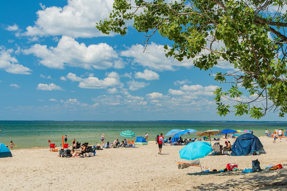 Una playa con gente, tiendas de campaña y sombrillas bajo un cielo despejado.