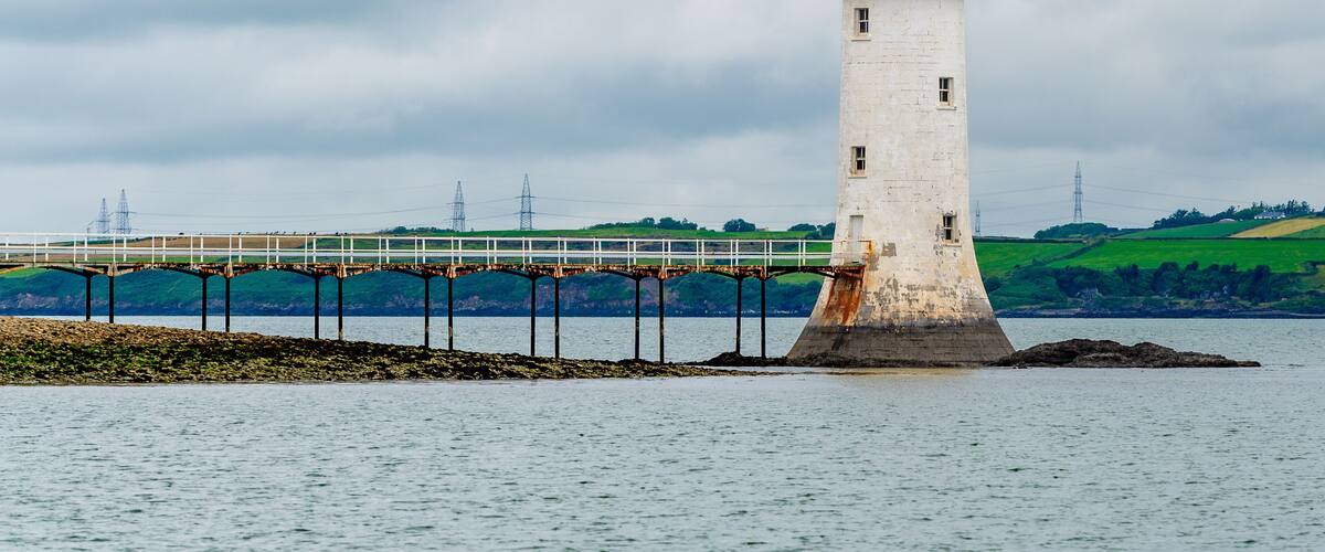 A lighthouse on a small island with a bridge in the background.
