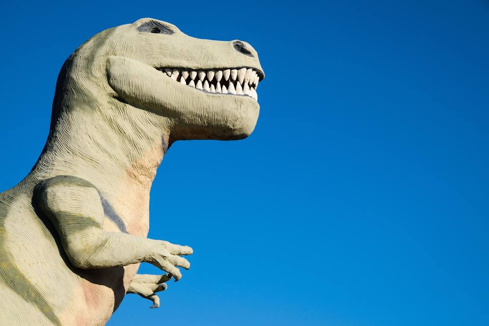 Uma grande estátua de dinossauro com cabeça proeminente e boca aberta.