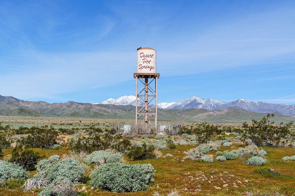 Un château d’eau portant l’inscription « Desert Hot Springs » se dresse dans un paysage désertique, avec des montagnes en arrière-plan.