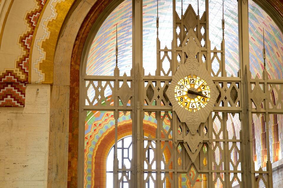 A large, ornate clock with intricate patterns and a colorful stained glass window in the background.
