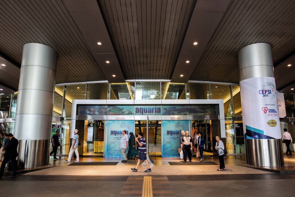 A modern building entrance with large glass doors, a prominent aquarium sign, and a vertical banner with CEPSI 2018 branding.