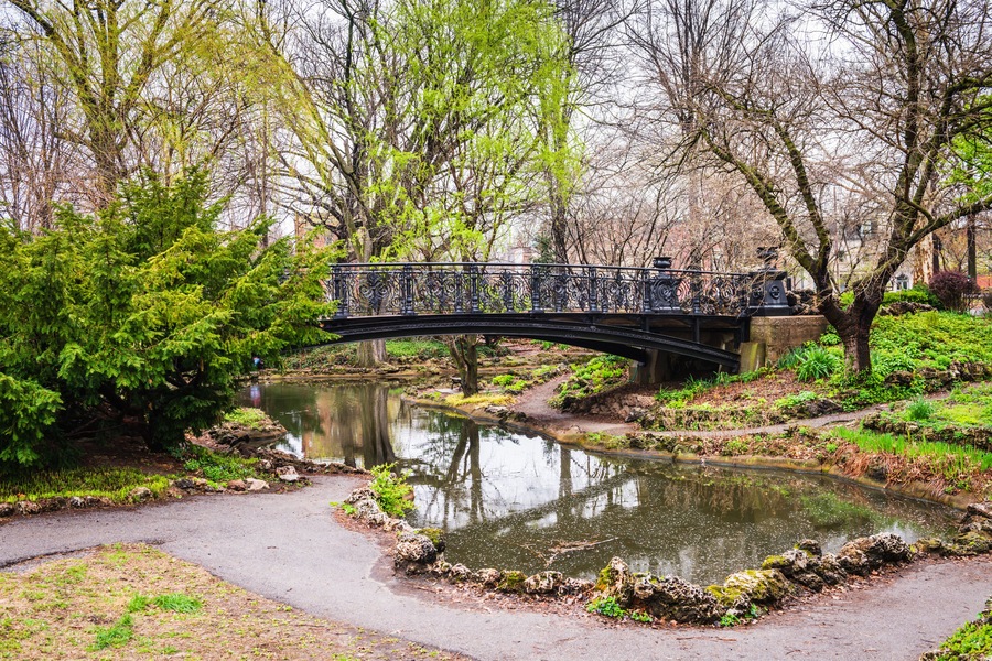 A stone bridge over a pond surrounded by trees and greenery.