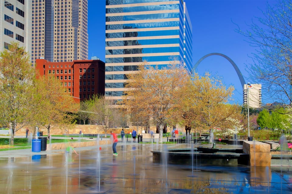A city park with a fountain, trees, and modern buildings in the background.