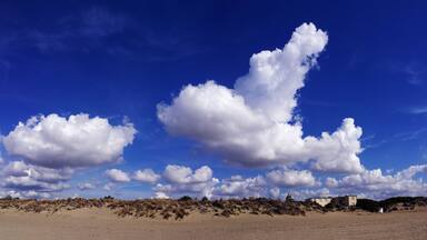 A beach with sand dunes and a clear blue sky with clouds.