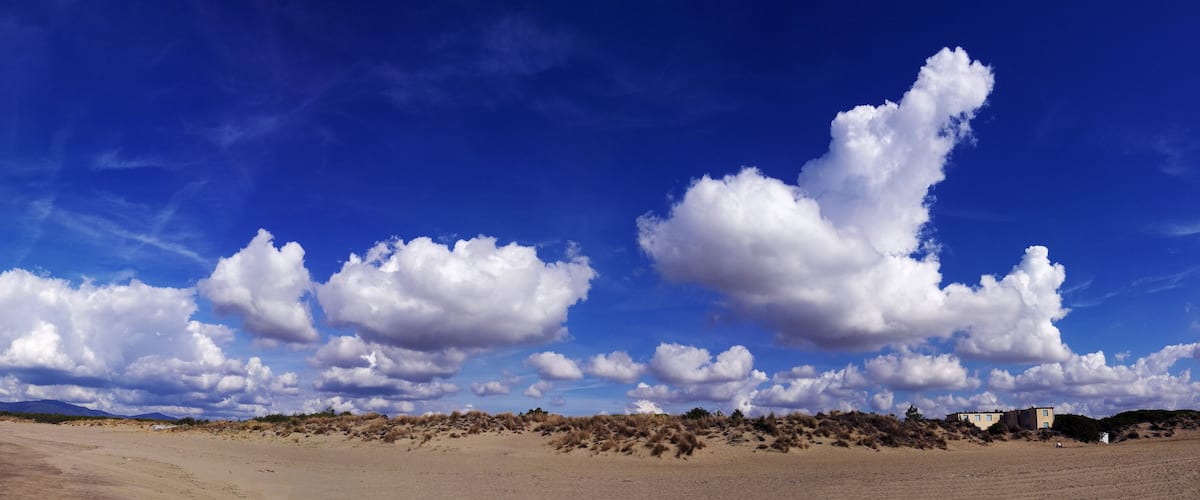A beach with sand dunes and a clear blue sky with clouds.