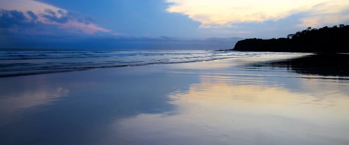 A beach with calm waves, a clear sky, and a distant shoreline.