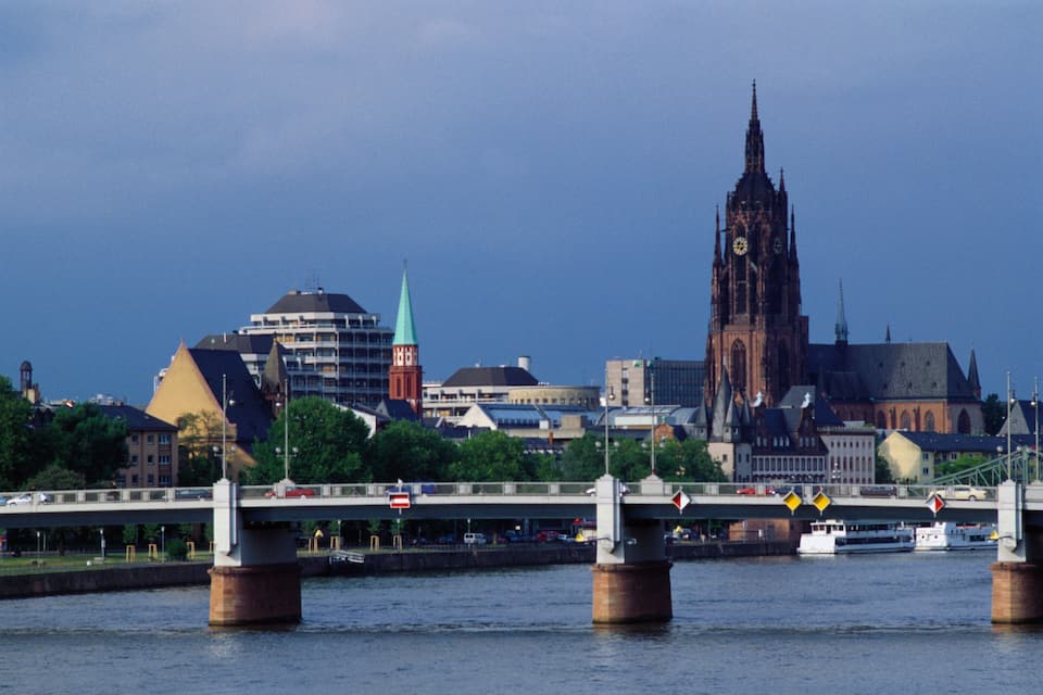 A city skyline with a prominent church tower, a bridge with vehicles, and a river.