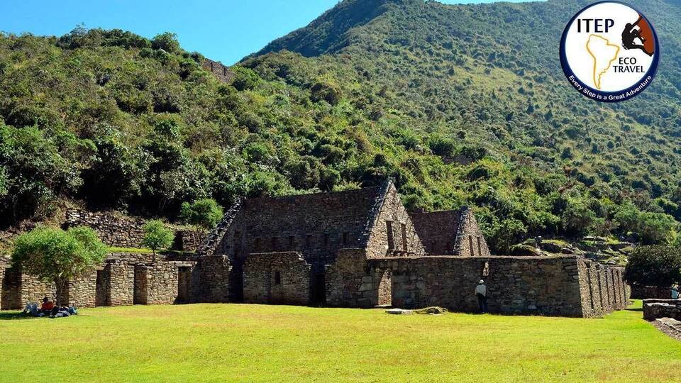 A stone building surrounded by lush greenery and a mountain in the background.