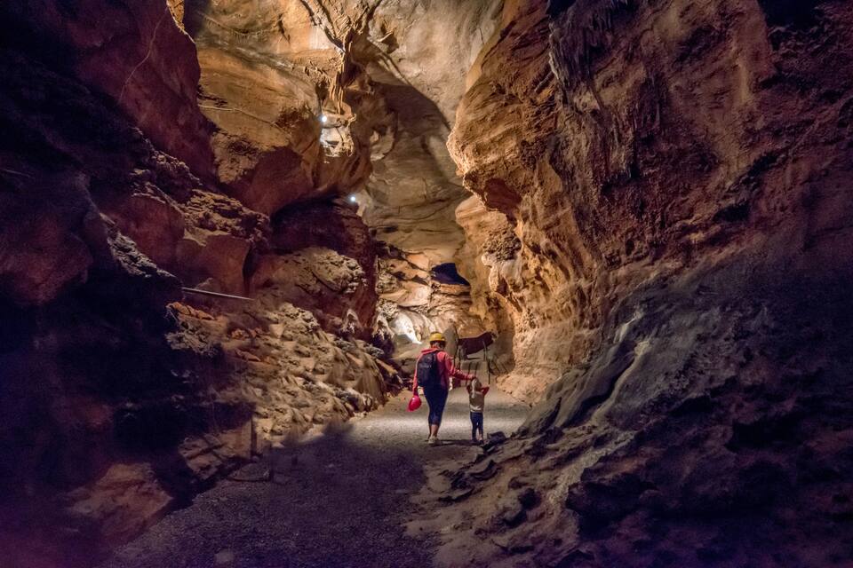 Un estrecho pasaje cavernoso con paredes rocosas y una persona caminando con un niño.