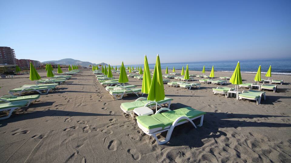 A beach with rows of green and white sun loungers and umbrellas.