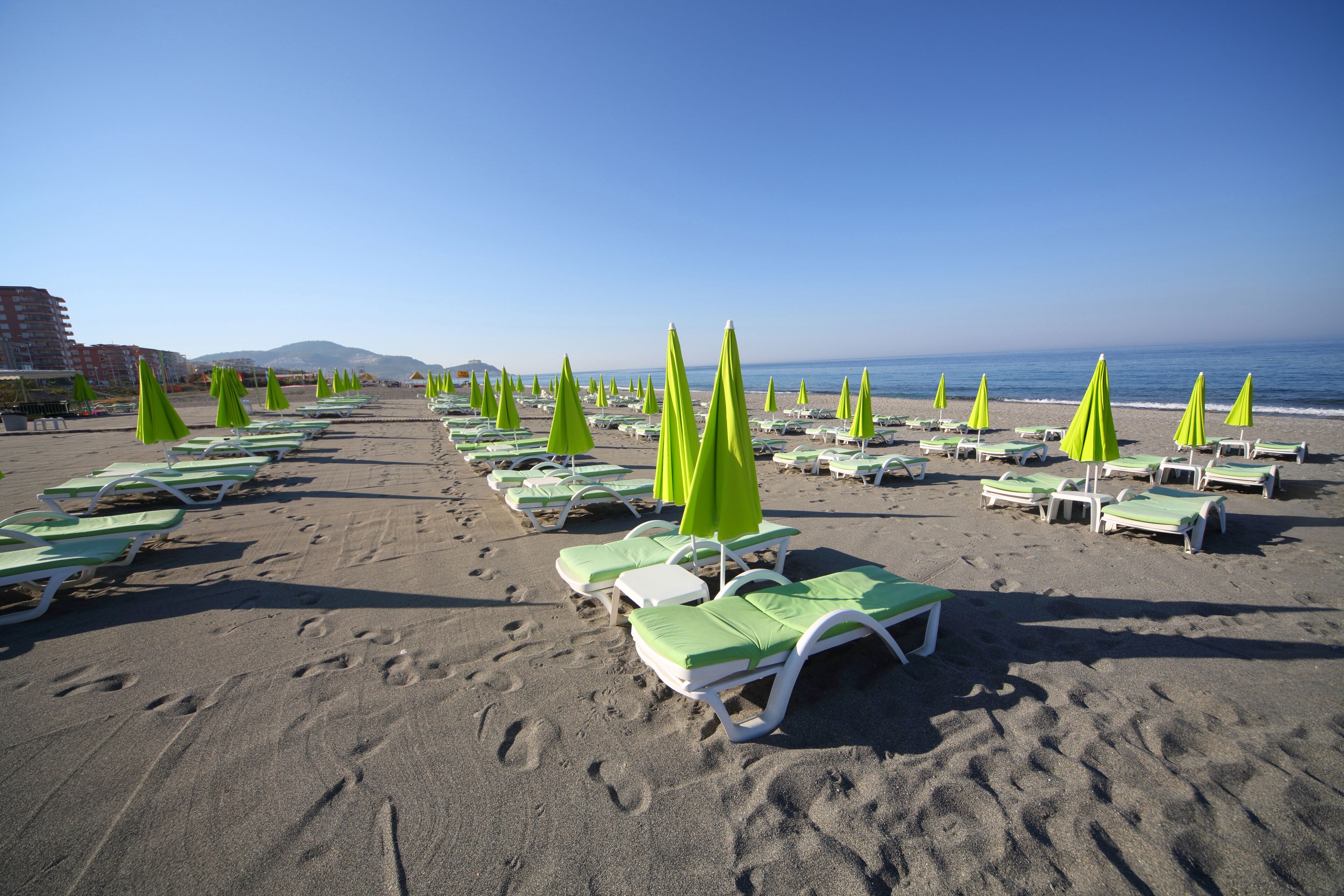 A beach with rows of green and white sun loungers and umbrellas.