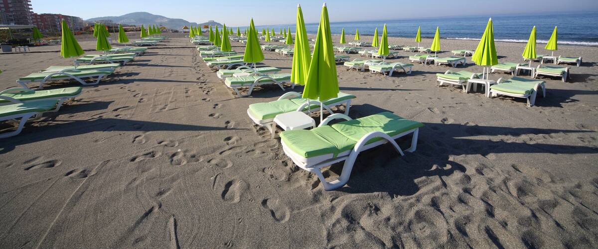 A beach with rows of green and white sun loungers and umbrellas.