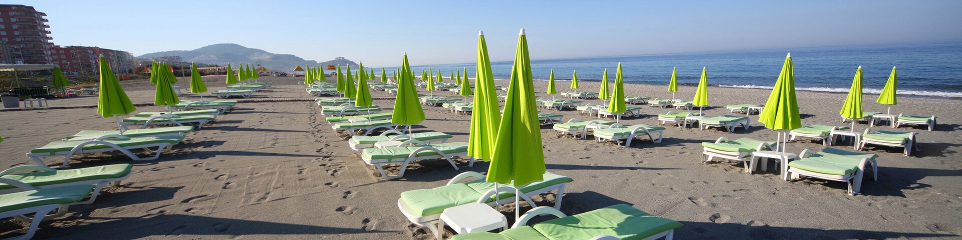 A beach with rows of green and white sun loungers and umbrellas.