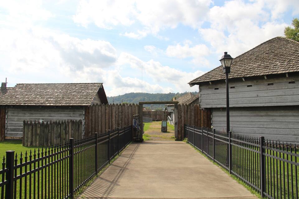 A wooden building with a black metal fence and a paved walkway leading to a gate.