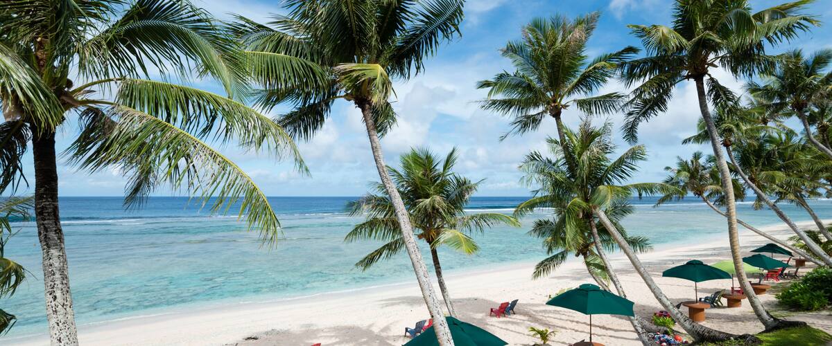 Coco Palm Garden Beach in Guam, USA. There are beach umbrellas, chairs on the white sand and palm trees on the beach contiguous to the coral reef with transparent water. ; Shutterstock ID 542043004; P
