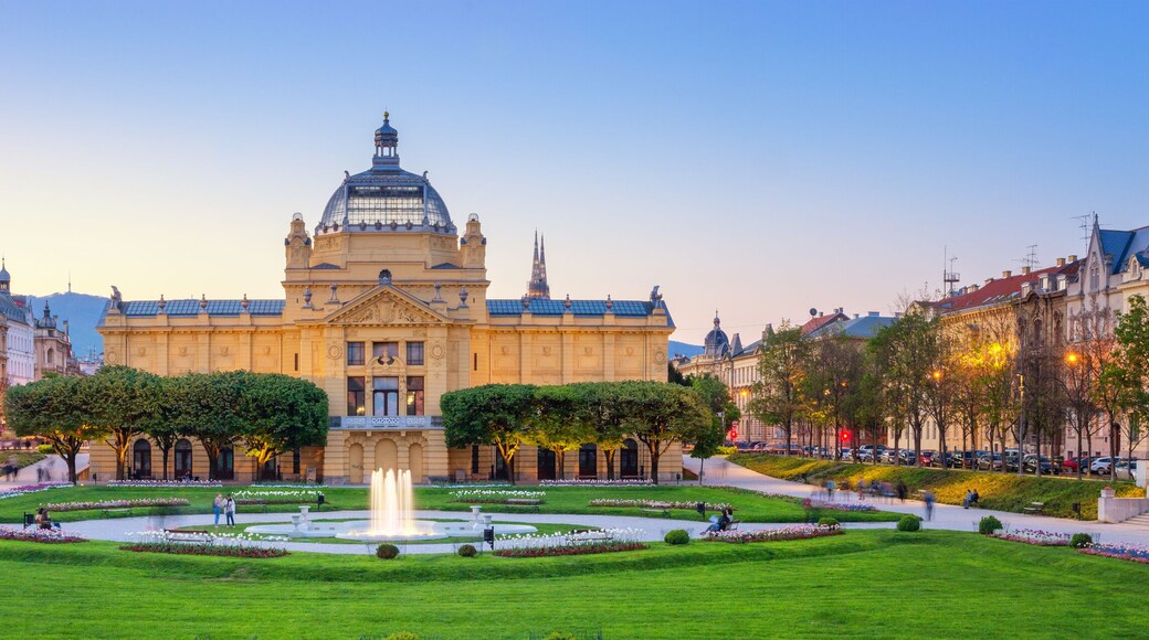 A grand building with a dome and a fountain in the center of a well-manicured garden.