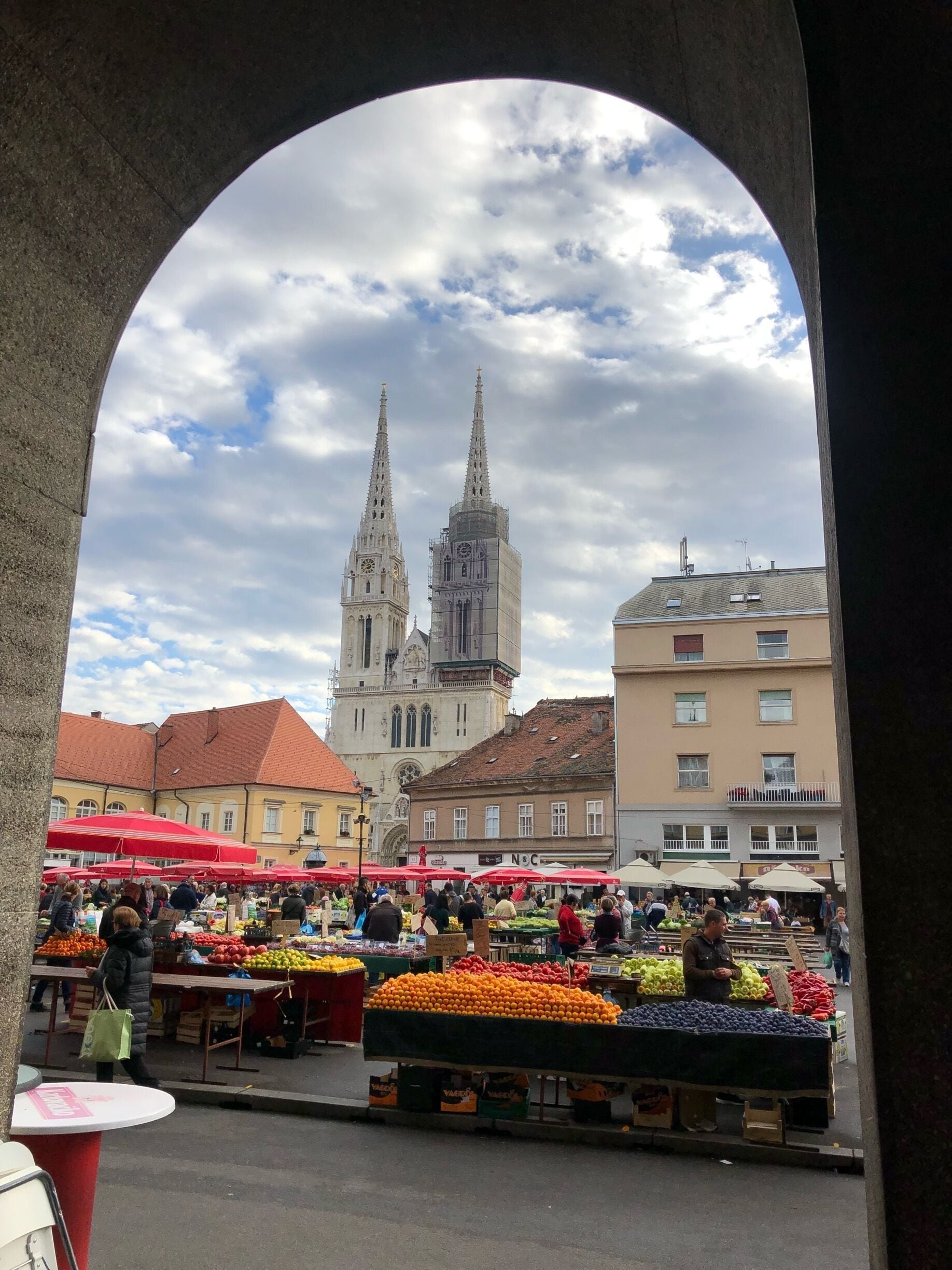 Un marché avec des étals de fruits et, en arrière-plan, une église historique dotée de deux flèches.