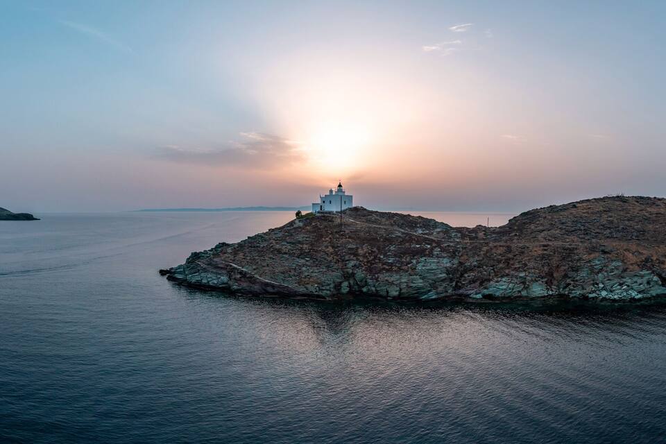 Un phare sur une île rocheuse, avec des eaux calmes et un ciel dégagé.