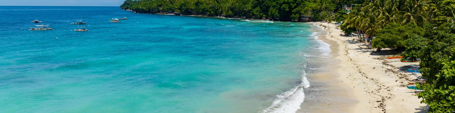 White sandy beach with turquoise sea water and waves. Samal Island. Davao, Philippines.