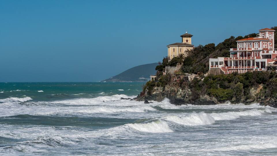 A coastal town with a lighthouse and buildings on a cliff overlooking the ocean.